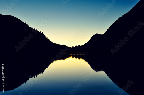 View of Fedaia reservoir lake (Lago Fedaia) at dawn near Marmolata mountain, the highest peak of the Dolomites Mountains in the province of Trentino, South Tyrol, Italy. Photo cross processed.