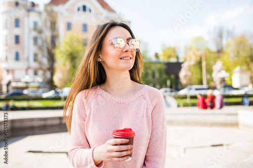 Summer sunny lifestyle fashion portrait of young stylish woman walking on street, wearing cute trendy outfit, drinking hot drink, smiling enjoy weekends. photo