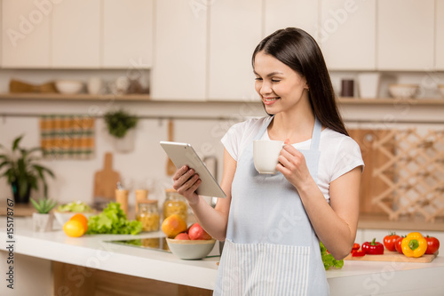 Young Woman in kitchen with tablet computer looking recipes  smiling. Food blogger concept