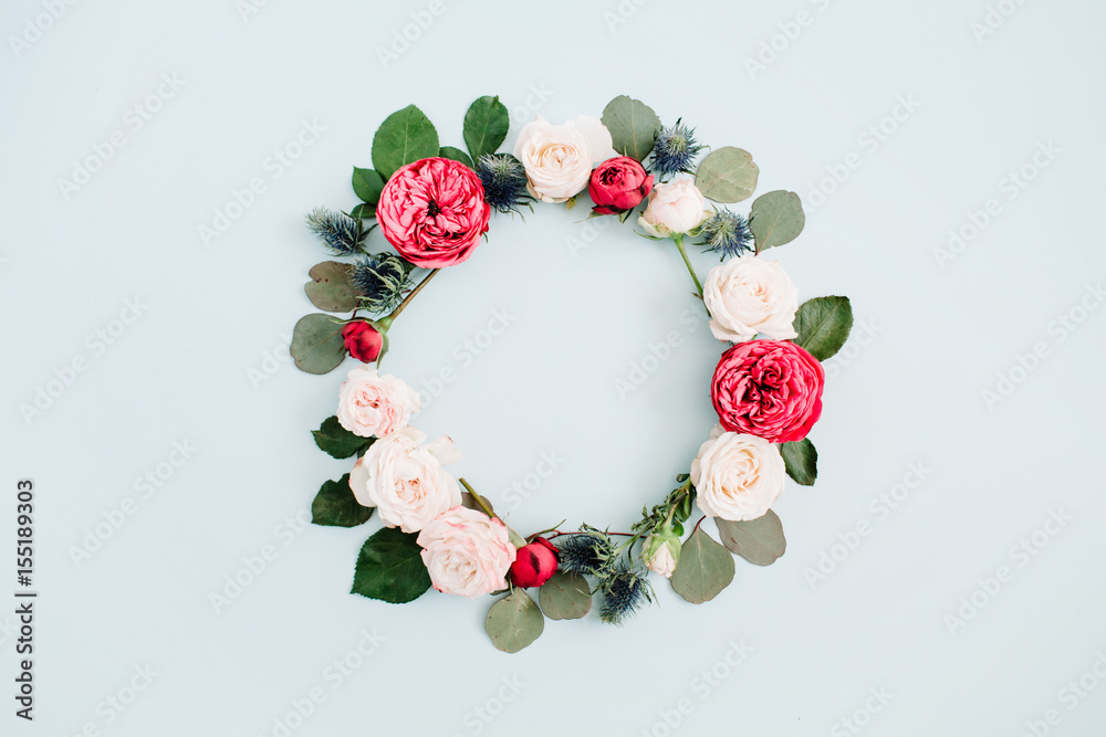 Flower frame wreath made of beige and red roses, eucalyptus branches on pale pastel blue background. Flat lay, top view. Floral texture background.
