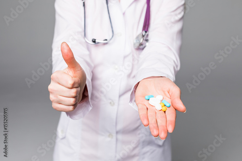 Woman nurse showing pill in hand isolated on grey