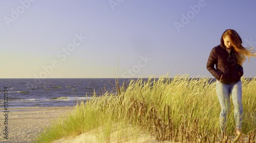Girl spending free time on seashore. Young long hair woman walking on sandy beach dunes in summer cold windy day 4K ProRes HQ codec