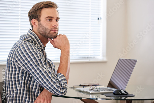 Young man resting his head on his hand while looking into the distance, day dreaming to procrastinate and get out of having to get back to work and study.