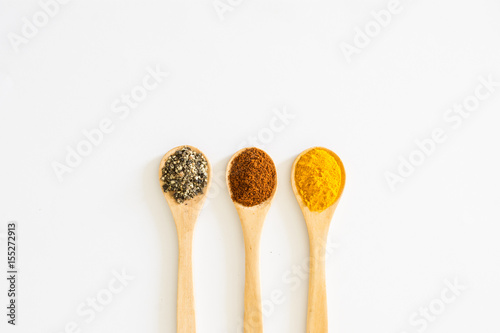 Turmeric, Paprika and Black Pepper in wooden spoon over white background.