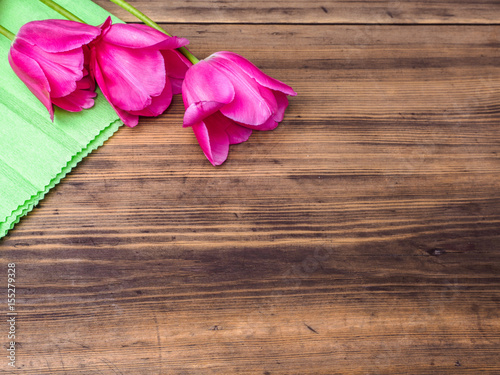 Pink tulips, floral arrangement on wooden background with green paper and space for message. Background for Mother's Day, 8 March and other greeting cards or invitations for lovely women. Soft focus.