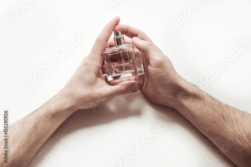 Мужские руки с стеклянным флаконом духов на белом фоне