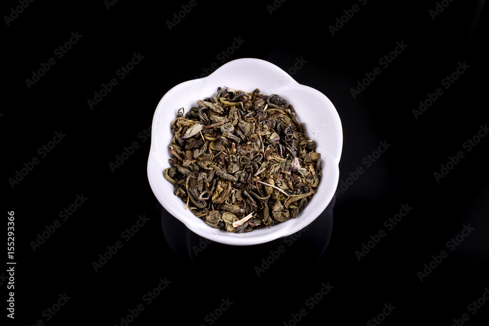 Green and black tea leaves in ceramic bowl on black background Green and black tea leaves in ceramic bowl on black background