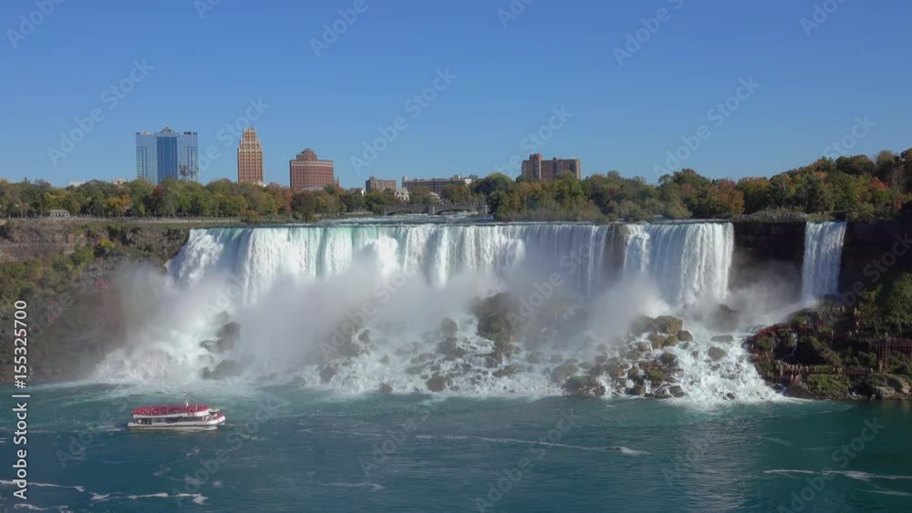 View of tour boat cruising at the base of misty Niagara Falls as seen from the Skylon Tower. Whitewater waterfalls American & Bridal Veil Falls, touristic hotels and New York skyline in the background View of tour boat cruising at the base of misty Niagara Falls as seen from the Skylon Tower. Whitewater waterfalls American & Bridal Veil Falls, touristic hotels and New York skyline in the background