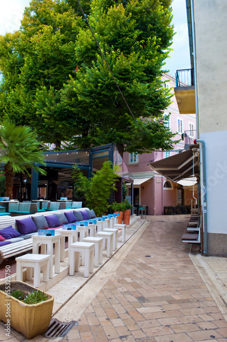 Cozy and empty narrow street on a summer morning. Small cafe with chairs, a couch and many colorful pillows under the canopy of high green trees. Zadar center, Croatia