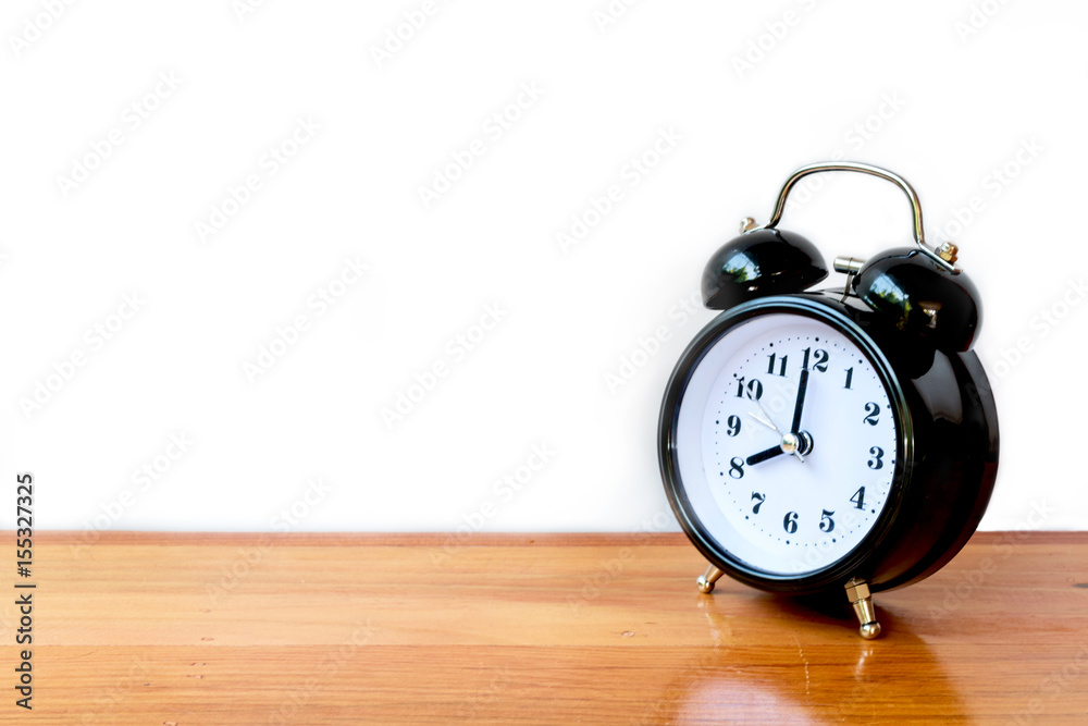 The alarm clock at 8.00 o'clock, black color, on the wood table, white background The alarm clock at 8.00 o'clock, black color, on the wood table, white background