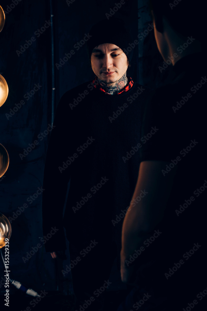 Fototapeta premium male hipsters in tattoos in black clothes, looks down on a dark background, the reflection