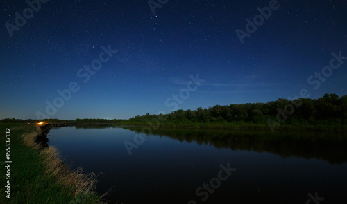 The stars in the night sky are reflected in the river. The landscape is photographed by moonlight. © olgapkurguzova