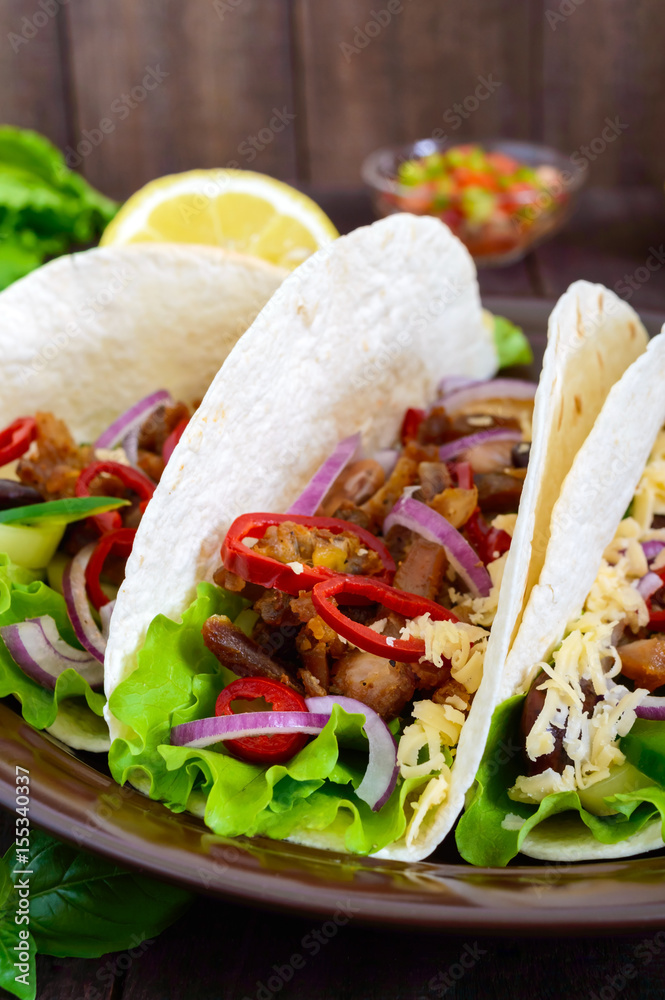Tacos is a traditional Mexican dish. Tortilla stuffed with chicken, bell and hot peppers, beans, lettuce, cheese, blue onion with salsa sauce on dark wooden background. Vertical view Tacos is a traditional Mexican dish. Tortilla stuffed with chicken, bell and hot peppers, beans, lettuce, cheese, blue onion with salsa sauce on dark wooden background. Vertical view