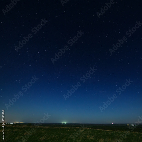 Stars in the night sky with city lights on the horizon. The landscape is photographed by moonlight.