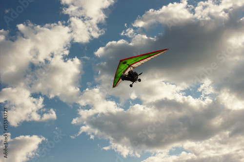 The motorized hang glider flying on background blue sky with clouds.
