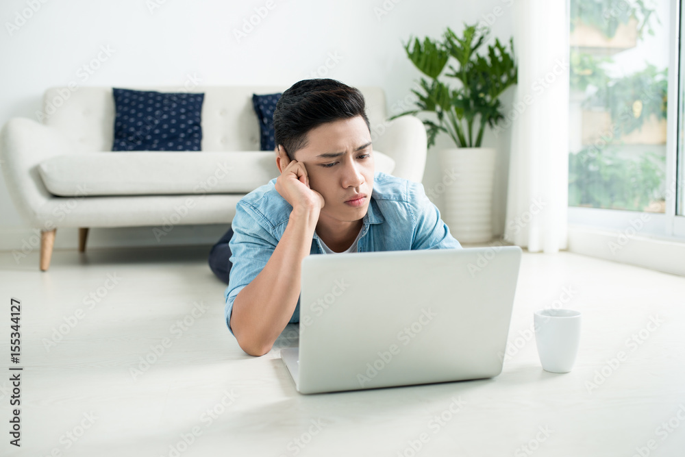 Asian man lying on the floor with laptop and coffee. Asian man lying on the floor with laptop and coffee.