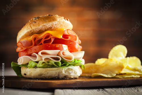 Delicious sandwich with ham, lettuce, tomato, chicken and cheddar cheese on a wooden table