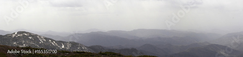Panoramic landscape with peaks of mountains, hills, forest and sky with contrasting clouds