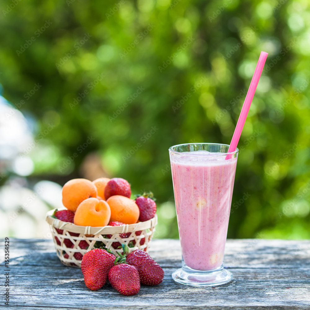 Wicker basket with strawberries and apricots, glass with strawberry smoothies, natural wood background Wicker basket with strawberries and apricots, glass with strawberry smoothies, natural wood background