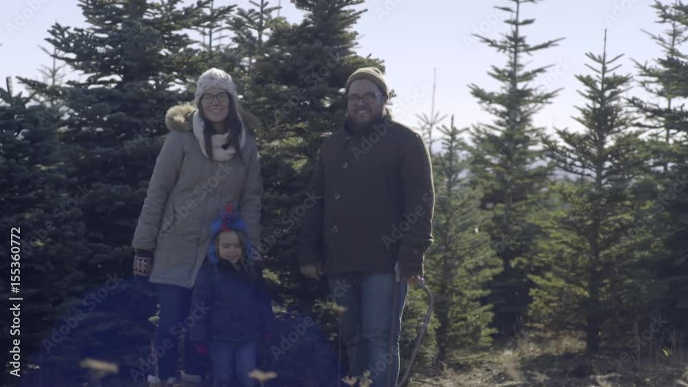 Happy Young Family Smile And Pose With Their Christmas Tree, Before They Cut It Down Happy Young Family Smile And Pose With Their Christmas Tree, Before They Cut It Down