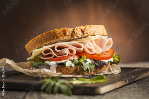 Tasty sandwich with ham, cheese, tomato and lettuce on wooden background