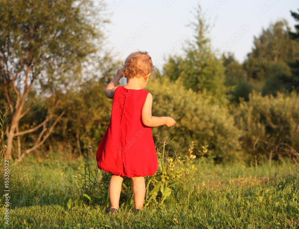 Adorable little girl in bright red dress walking in the summer park