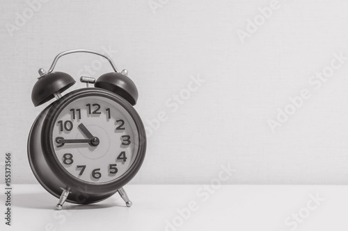 Closeup alarm clock for decorate show a quarter to eleven o'clock or 10:45 a.m. on white wood desk and cream wallpaper textured background in black and white tone with copy space