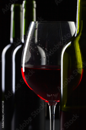 Bottles and glass of red wine on a black background .