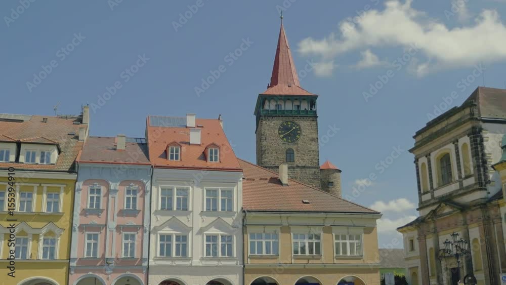 Sunny medieval Renaissance square with stone tower and clock. View to row of houses with colorful old facades and blue sky. Age-old gas lamp and arcades. Static day shot, color corrected footage.