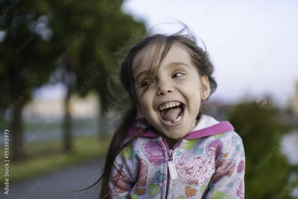 Little girl in european city sitting on the bench andplay with emotions. Portrait of caucasian kid enjoy summer evening