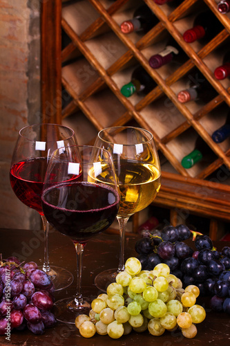Glasses of red  rose and white wine with cheese  and grape in wine cellar.  Food and drinks concept