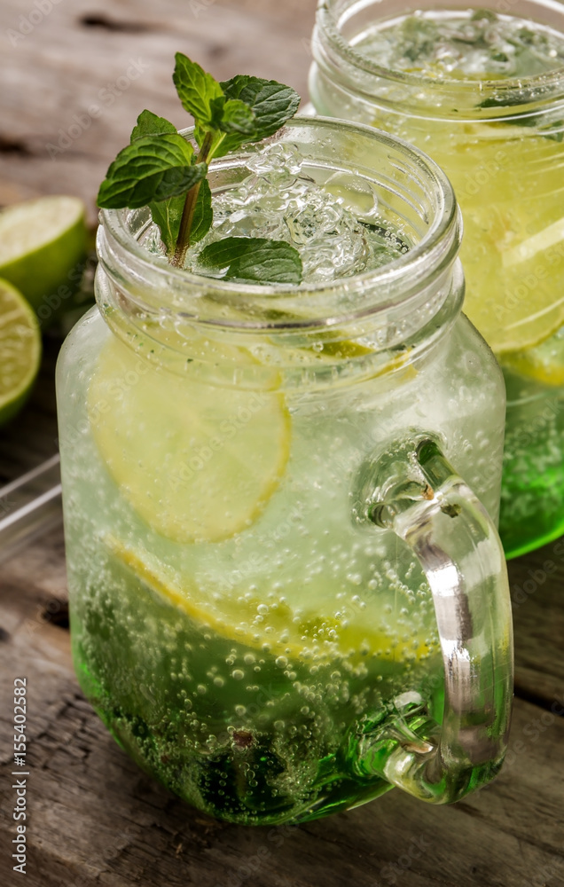 Tasty cold fresh drink lemonade with lemon, mint, ice and lime in glass on wooden table. Closeup. Tasty cold fresh drink lemonade with lemon, mint, ice and lime in glass on wooden table. Closeup.