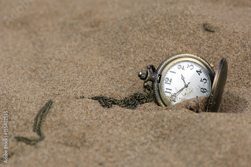round pocket watch on a chain in the sand