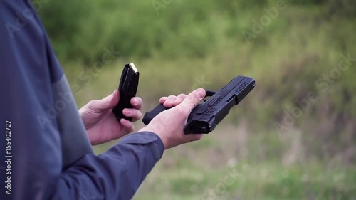 Male hand holding gun, reloading it and shooting from it on a field shooting