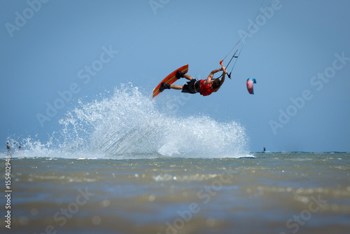 Recreational water sports: kite surfing. Kite boarding sportsman jumping high in the sky on windy day