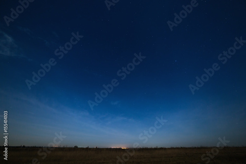 Stars in the night sky with city lights on the horizon. The landscape is photographed by moonlight.