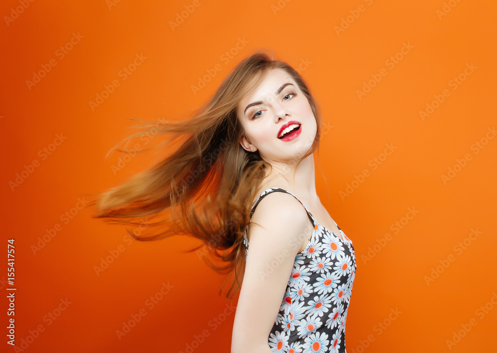 Active Young Woman with Long Dark Hair Wearing Dress with Flowers is Having Fun in Studio While Posing on Orange Background. Hair Style Concept. Active Young Woman with Long Dark Hair Wearing Dress with Flowers is Having Fun in Studio While Posing on Orange Background. Hair Style Concept.