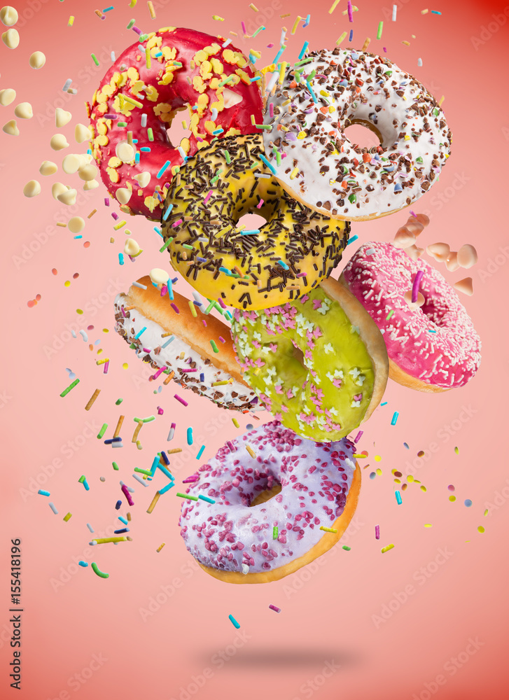 Tasty doughnuts in motion falling on pastel red background.