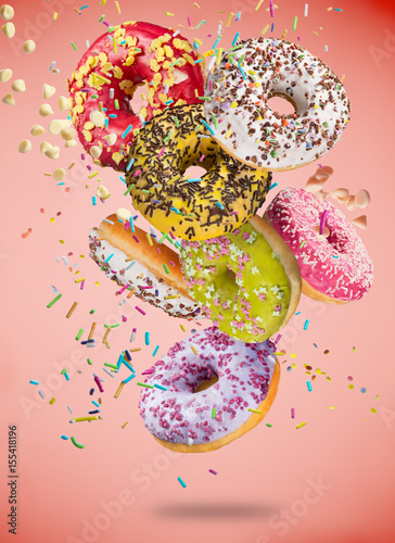 Tasty doughnuts in motion falling on pastel red background.