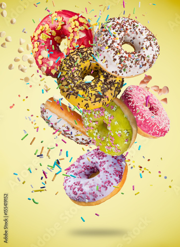Tasty doughnuts in motion falling on pastel yellow background.