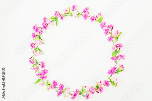 Floral round frame made of pink flowers and leaves on white background. Flat lay, top view.