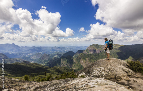 man with backpack standing on top of mountain with blue sky with clouds