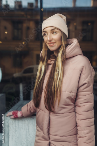 The beautiful girl in a pink jacket and a cap in cafe. She lovely smiles and looks out of the window. At the girl beautiful long hair.