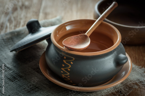 Clay pot for baking with lid with wooden spoon on linen napkin on dark background