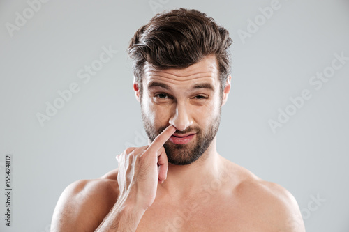 Portrait of a young bearded naked man picking his nose photo