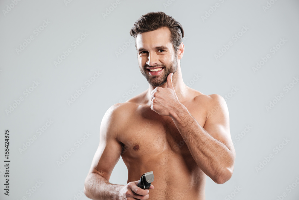 Handsome young man holding electric razor and touching his chin Handsome young man holding electric razor and touching his chin