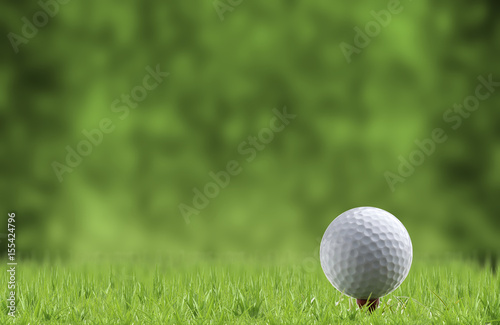 Golf ball and tee on green grass, isolated against the green blurred background.