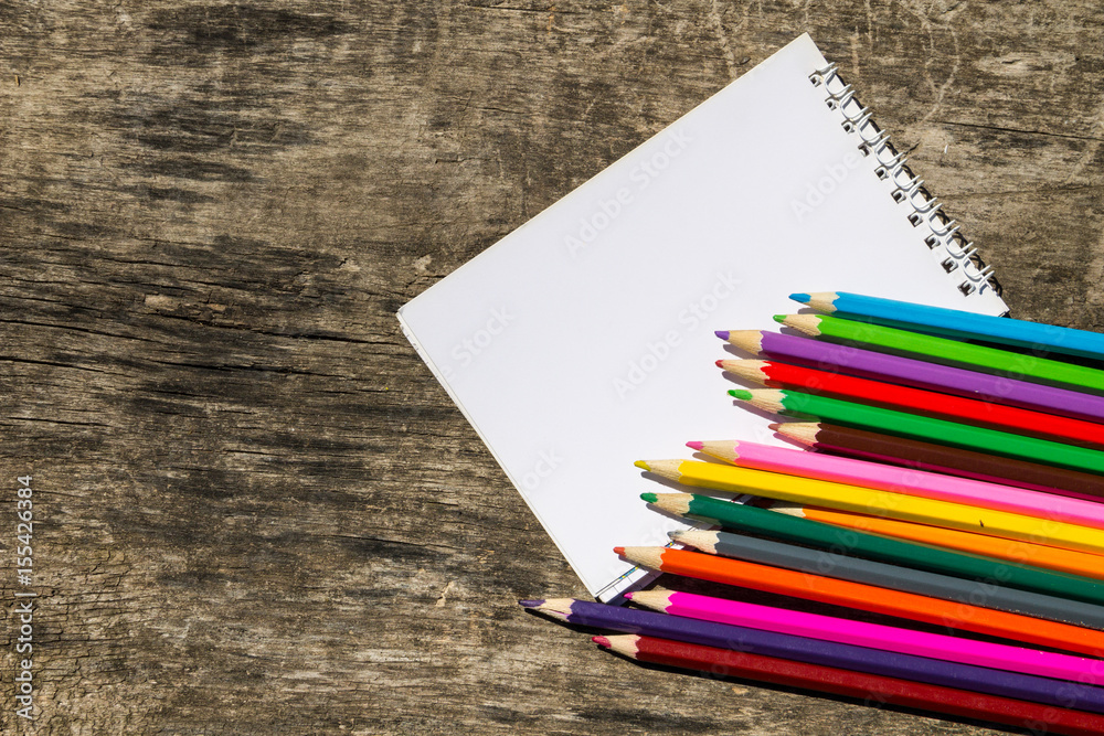 Colored pencils and blank notepad on old wooden desk Colored pencils and blank notepad on old wooden desk