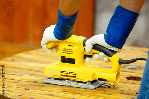 Close up of a man using an electric sander on pine floor or table sanding surface photo