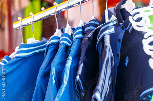 Baby clothes pants t-shirts sweaters shirts hanging on hangers in a shop outside in sunny weather photo